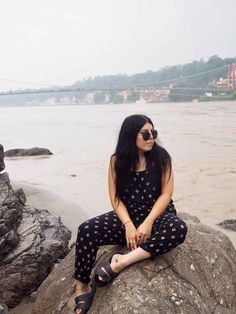 a woman sitting on top of a rock near the water