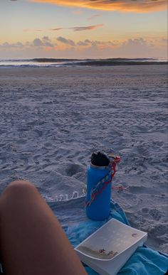 a person laying in the sand with a blue water bottle on their lap at sunset