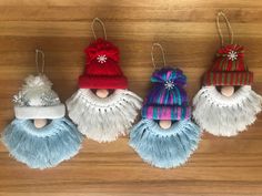 three ornaments are hanging on a wooden surface, one is wearing a hat and the other has a knitted cap