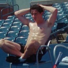 a shirtless man sitting on the bleachers at a baseball game with his hands behind his head