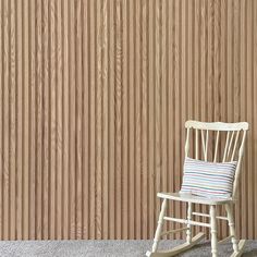 a white rocking chair sitting in front of a wooden wall with vertical slats on it