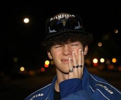 a young man wearing a hat and blue jacket is holding his hand up to his face