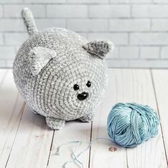 a stuffed animal next to a ball of yarn on a wooden floor with a brick wall in the background