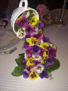 purple and yellow pansies are in a white vase on a table with silverware