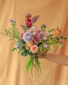 a woman holding a bouquet of flowers in her hand on a yellow background with pink, purple and orange colors