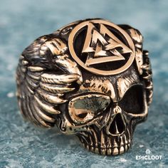 a skull ring with an inverted triangle on it's head and wings around the band