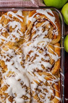 a pan filled with cinnamon rolls covered in icing next to some green apple's