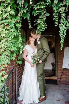 a bride and groom kissing in front of an ivy covered doorway at the end of their wedding day