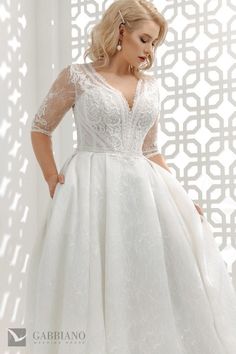 a woman in a white wedding dress standing against a wall with her hands on her hips