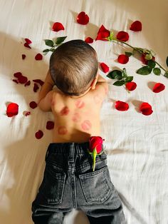 a young boy laying on top of a bed covered in rose petals with his back to the camera