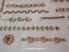 some pink flowers and green leaves are on a white tablecloth with stitched edges