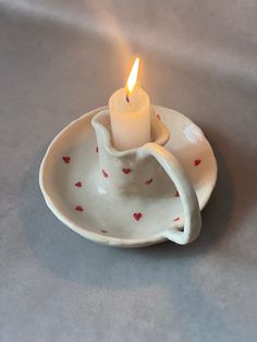 a lit candle in a small white dish on a gray tablecloth with red hearts