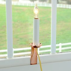 a white candle sitting on top of a window sill next to a green field