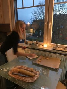 a woman standing at a table in front of a window with food on top of it