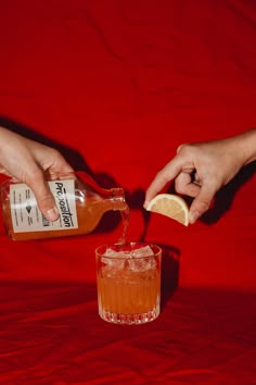 two hands are pouring an orange juice into a glass with a slice of lemon on the rim