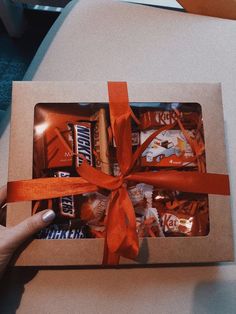 someone is holding an open box with candy and candies wrapped in orange ribbon around it