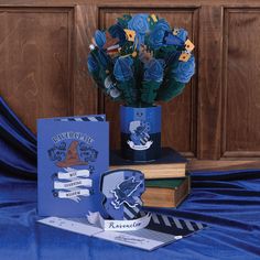 blue roses are in a vase next to two greeting cards and a book on a table