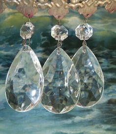 three pairs of crystal earrings hanging from a chandelier in front of a painting