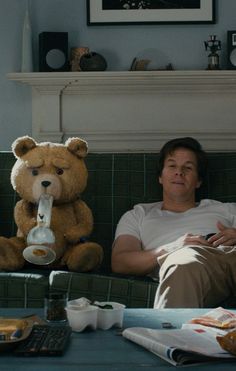 a man sitting on a couch next to a teddy bear