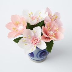 pink and white flowers in a blue vase on a white table top with green leaves