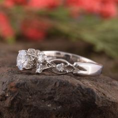 a close up of a ring on top of a rock with flowers in the background