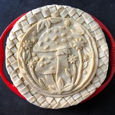 an intricately decorated pie sitting on top of a red pan filled with fruit and vegetables