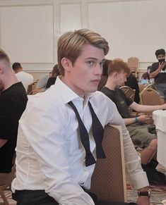 a young man sitting at a table with other people in the background wearing formal attire