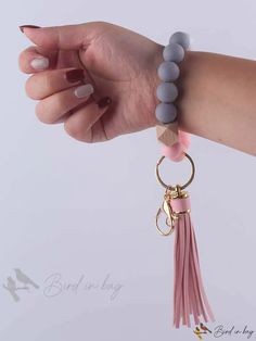 a woman's hand holding onto a pink and grey bracelet with tassels