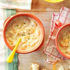 two orange bowls filled with soup on top of a wooden table next to some bread