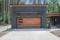 a modern garage with wood and metal doors in front of it, surrounded by trees