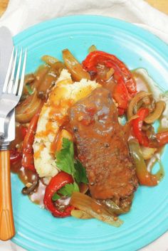 a blue plate topped with meat and veggies covered in gravy next to two forks