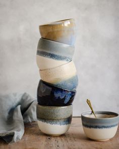 a stack of ceramic cups sitting on top of a wooden table next to a bowl