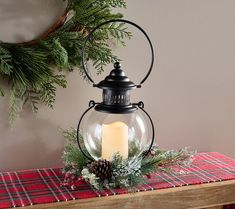 a candle is lit in a glass lantern on a table next to a christmas wreath