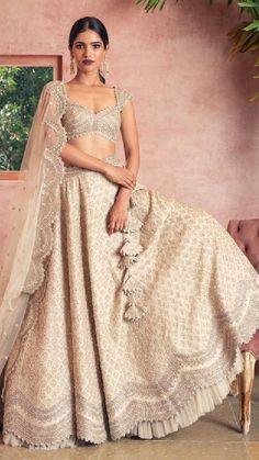 a woman in a white and gold lehenga sitting on a pink chair with her hand on her hip