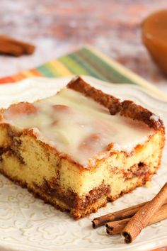 a piece of cake sitting on top of a white plate next to cinnamon sticks and an orange bowl