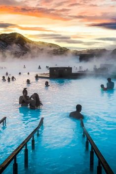 many people are swimming in the blue lagoon at sunset or dawn, with steam rising from the water