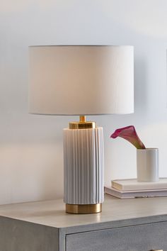 Simple and Elegant. This column ceramic table lamp is finished with a ridged detailing and white colourway. Encased top and bottom with a contrasting gold metal and finished with a faux cotton self lined white shade for ultimate understated glamour. Also available in other colours. Wipe clean only. 90% Ceramic, 5% Cotton, 5% PVC. Gold And White Lamp, Bachelorette House, Minimal Table Lamp, Bed Side Table Lamp, White Bedside Lamps, Cream Lamp, White Lamps, Gold Metal Table, Side Table Lamp