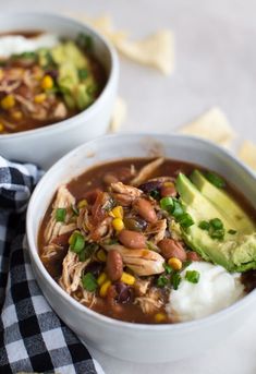 two white bowls filled with chili, beans and avocado next to tortilla chips