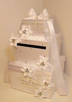 three tiered wedding cake with white flowers and ribbons on the top, sitting in front of a wall