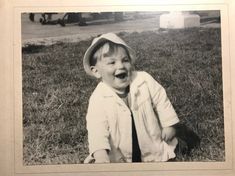 an old photo of a young boy sitting in the grass with his mouth open and tongue out