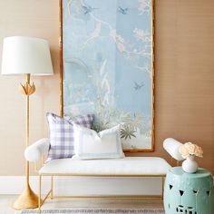 a white couch sitting next to a blue vase on top of a wooden table in front of a painting