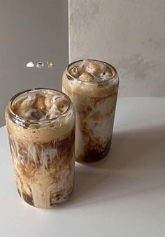 two glasses filled with iced coffee sitting on top of a white table next to each other