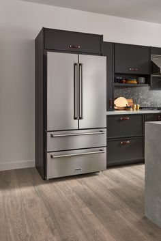 a stainless steel refrigerator in a kitchen with black cabinets and wood flooring on the walls