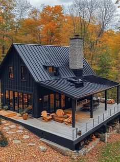 a black house with a deck and chairs on the front porch surrounded by fall foliage