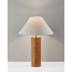 a wooden table lamp with a white shade on the top and bottom, in front of a gray wall