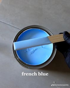 a person in black gloves is holding a paint can with blue liquid and a wooden spatula