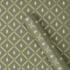 a green wallpaper with white trees on it and gold foil in the middle, next to a roll of wrapping paper