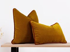 two yellow velvet pillows sitting on top of a wooden table next to a vase with flowers