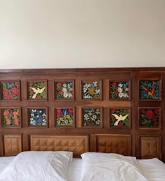 a bed with white sheets and pillows in front of a wooden headboard decorated with flowers