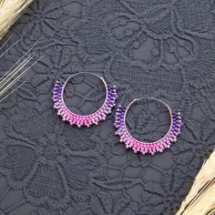 two pairs of purple and pink beaded hoop earrings on a black lace tablecloth